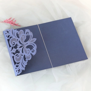 Detail of navy blue laser-cut lace wedding invitation on soft white fabric background