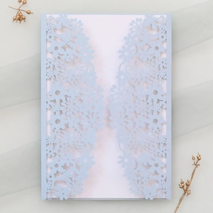 Detail of light blue laser-cut invitation featuring intricate hollow floral and butterfly patterns