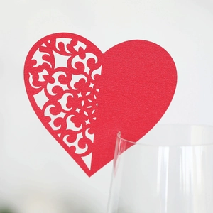 Detail of red heart laser-cut paper card placed on a glass for wedding table decor