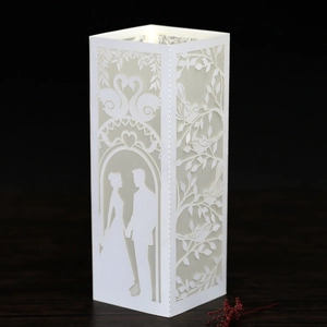 Close-up of white laser-cut paper candle bags with wedding couple and swan silhouette