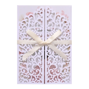 Detail of laser-cut wedding invitation with white hollow cover and beige satin ribbon bow
