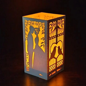 Detailed laser-cut pattern on white candle lantern with warm couple and birds silhouette