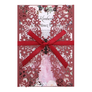 Detail of burgundy laser-cut floral wedding invitation with a red satin ribbon bow