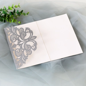 Close-up of laser-cut silver glitter lace invitation with elegant damask flower pattern