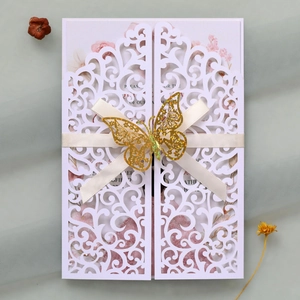 Detail of laser-cut wedding invitation with cream ribbon and gold glitter butterfly
