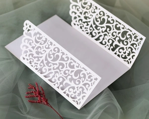 Detail view of white laser-cut wedding invitation featuring intricate filigree patterns