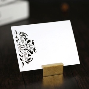 Golden metal place card holder with laser-cut white lace invitation on wood background