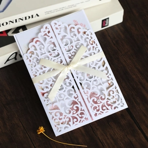Macro detail of laser-cut floral wedding invitation with cream ribbon bow on wood