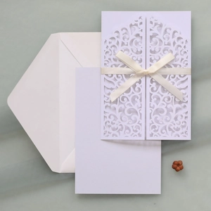Detail of laser-cut floral wedding invitation with cream silk bow and blank inner card