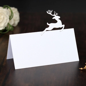 Macro shot of white hollow-out laser cut reindeer place card on dark wood table