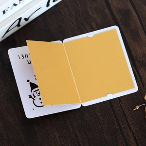 Close-up of laser-cut snowman Christmas card with yellow folding insert on wood surface