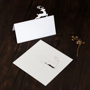 Detail of laser-cut white reindeer place cards on a dark wood table with golden floral accents