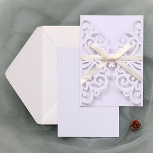 Laser cut white wedding invitation with elegant ribbon bow on textured gauze background