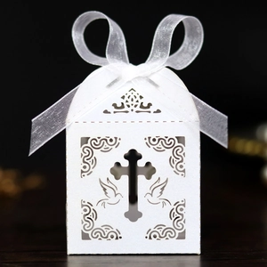 Detail of white laser-cut favor box with hollow cross, doves and white organza ribbon