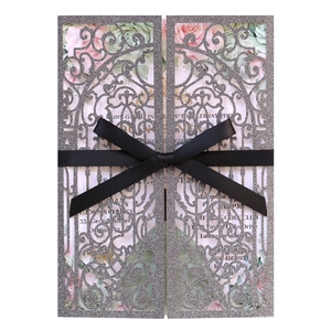 Detail of glitter laser cut wedding invitation with floral insert and black silk ribbon bow