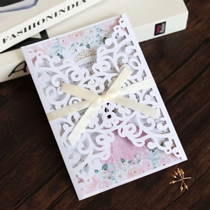Detail of laser-cut wedding invitation with intricate floral patterns and beige silk bow