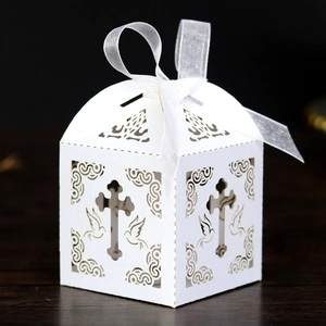Detail of laser-cut white cross favor box with doves and elegant white silk ribbon