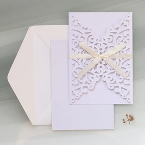 Detail of white laser-cut floral wedding invitation with cream satin ribbon and bow