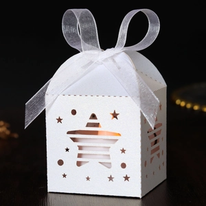 Detail of laser-cut star pattern gift box with white ribbon and warm glowing light
