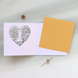 Macro shot of laser-cut heart patterns with bride and groom silhouettes on white card