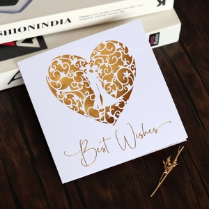 Macro detail of laser-cut gold heart with couple silhouette on white wedding card