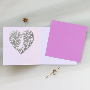 Detail of laser-cut heart floral pattern and couple silhouette on wedding invitation card