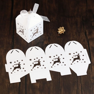 Laser-cut white Christmas favor box with reindeer cutout and ribbon on wood background