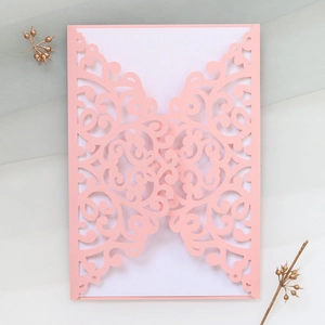 Detail of laser-cut light pink wedding invitation cover with intricate scroll patterns