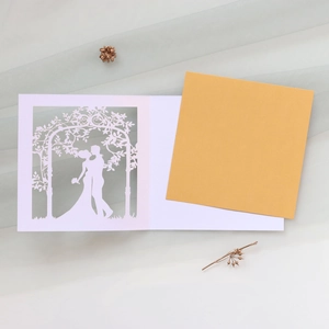 Macro shot of laser-cut wedding card with couple silhouette and floral arch details