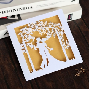 Detail of laser-cut white wedding invitation with gold lining and romantic couple silhouette