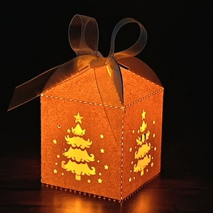 Detail of laser-cut Christmas tree patterns on a glowing orange paper candy gift box