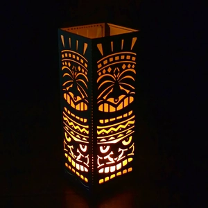 Tiki style black lantern with hollow tribal mask pattern and warm orange LED light glow