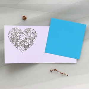Detail of laser-cut heart and floral hollow pattern on a white greeting card with blue insert