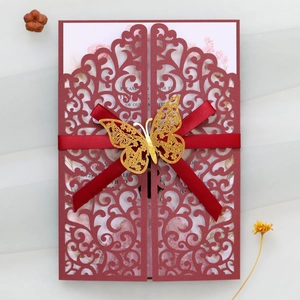 Detail of laser-cut wedding invitation with burgundy ribbon and gold butterfly charm