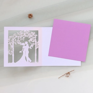 Detail of laser-cut wedding invitation showing a romantic couple under floral archway
