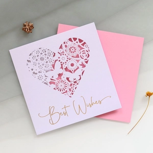 Close-up of laser-cut lace heart greeting card with gold Best Wishes foil and pink envelope