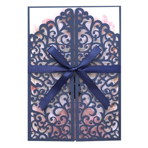 Detail of laser-cut navy blue wedding invitation with satin ribbon bow and floral insert