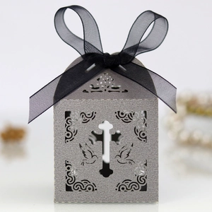 Close-up of laser-cut cross and dove patterns on white favor box with black organza ribbon