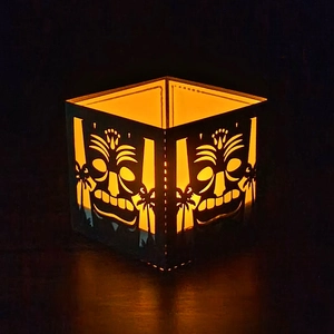 Detail of laser-cut Tiki mask lantern with tropical palm tree patterns and warm glow