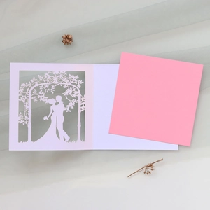 Detail of laser-cut wedding invitation featuring a romantic couple and floral archway
