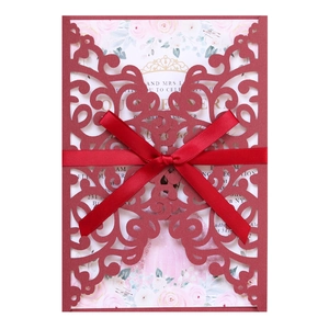 Detail of burgundy laser-cut invitation card with red ribbon bow and floral inner page