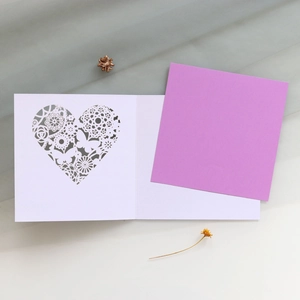 Detailed close-up of laser-cut heart and butterfly patterns on a white greeting card
