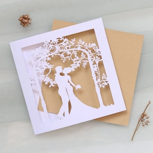 Detail of laser-cut wedding invitation showing a kissing couple and kraft envelope