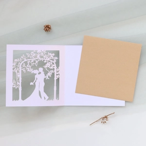 Detail of laser-cut wedding invitation featuring a couple silhouette and kraft envelope