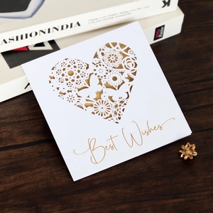 Detail of laser-cut lace heart greeting card with golden Best Wishes text on wood