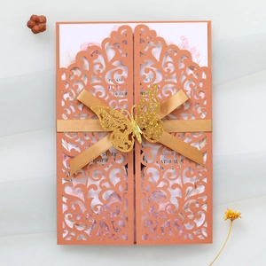 Detail of terracotta laser-cut wedding invitation with champagne ribbon and gold butterfly