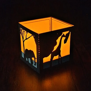 Close-up of black lantern featuring African giraffe and elephant silhouette with warm light