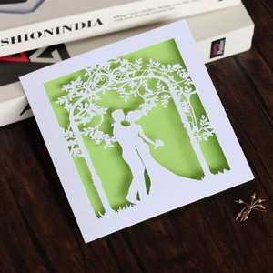 Macro detail of laser-cut wedding card featuring a romantic couple under a floral arch