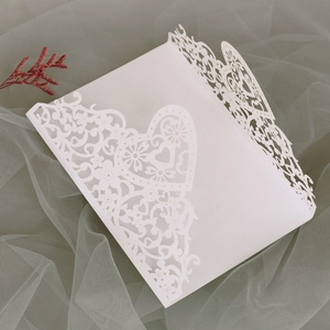 Macro shot of white laser-cut heart pattern wedding invitation on soft grey tulle