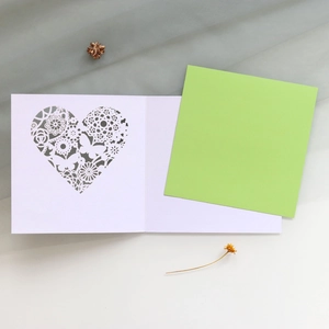 Detail of laser-cut butterfly heart invitation card with green liner on white desk